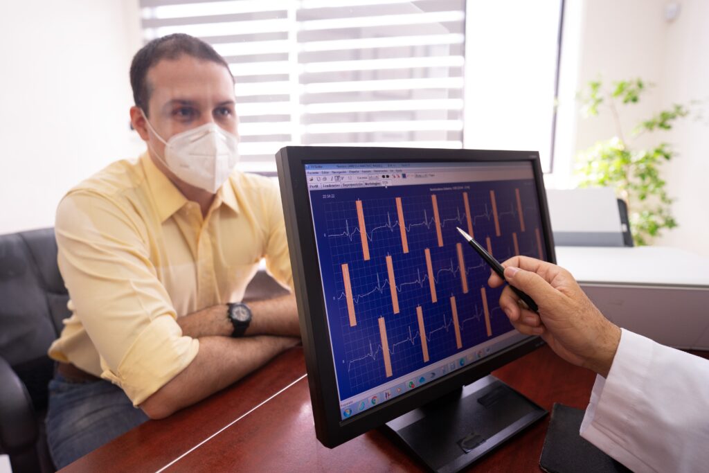 a cardiologist pointing to an ecg on desktop and talking to a patient